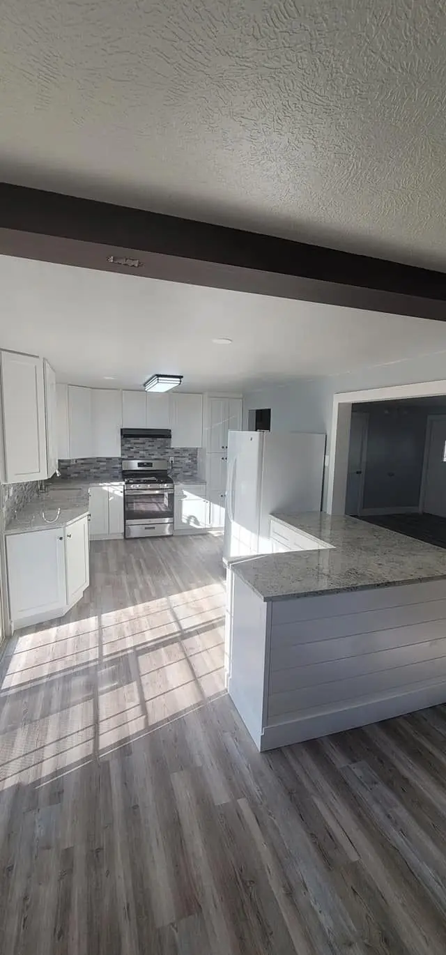 Kitchen with white cabinets, grey plank flooring and stone counters