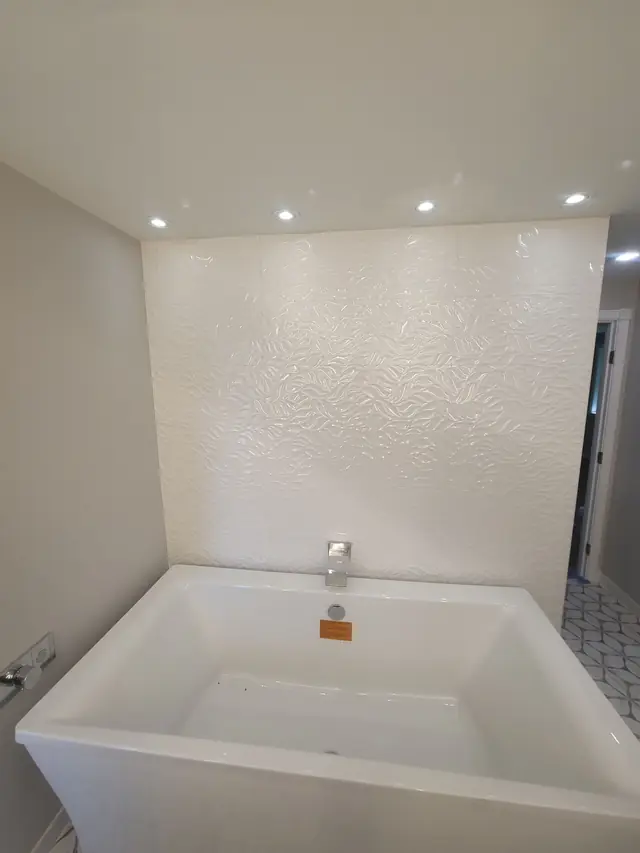 Freestanding soaking tub against a textured white tile wall